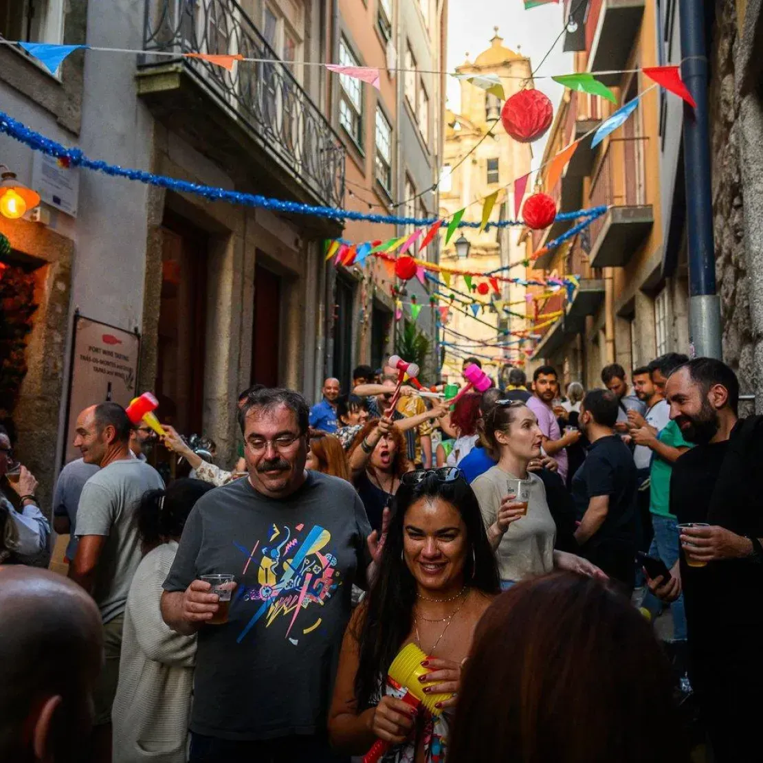 A imagem mostra uma rua estreita cheia de gente a celebrar uma festa popular. O ambiente é muito animado
