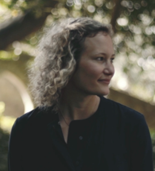 A imagem mostra uma mulher em ambiente exterior, iluminada por luz natural suave 