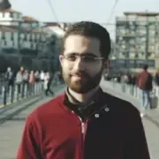 A imagem mostra um homem jovem ao ar livre, num ambiente urbano