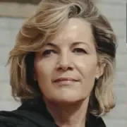 A imagem mostra uma mulher de meia-idade com cabelo loiro curto e volumoso, penteado de forma elegante