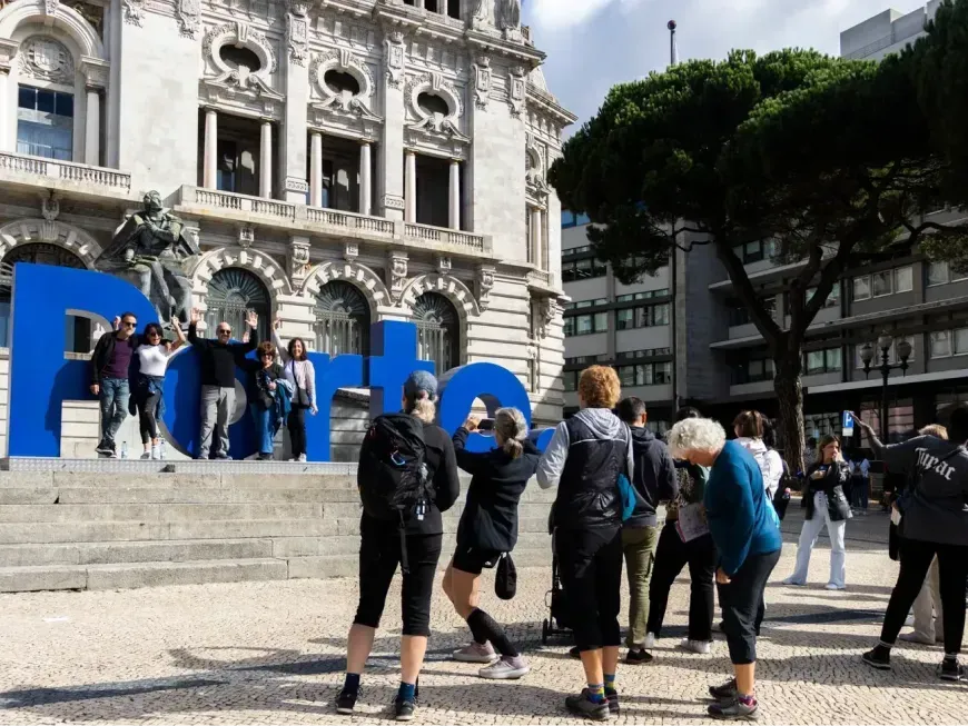 A imagem mostra um grupo de pessoas numa praça em frente a um edifício histórico, a Câmara Municipal do Porto